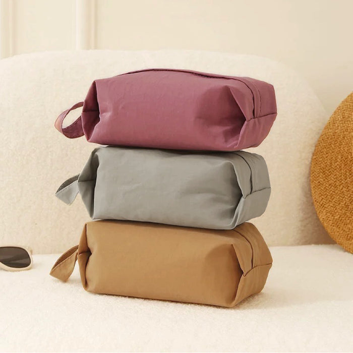 Stacked Soft Hue organizer bags in mauve, grey and tan; rectangular zip pouches with carry loops for tidy luggage.
