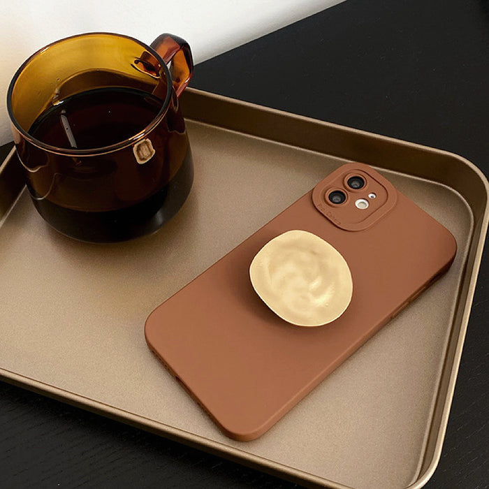 Brown silicone case with gold kickstand on a gold tray, reflecting a premium luxury lifestyle.