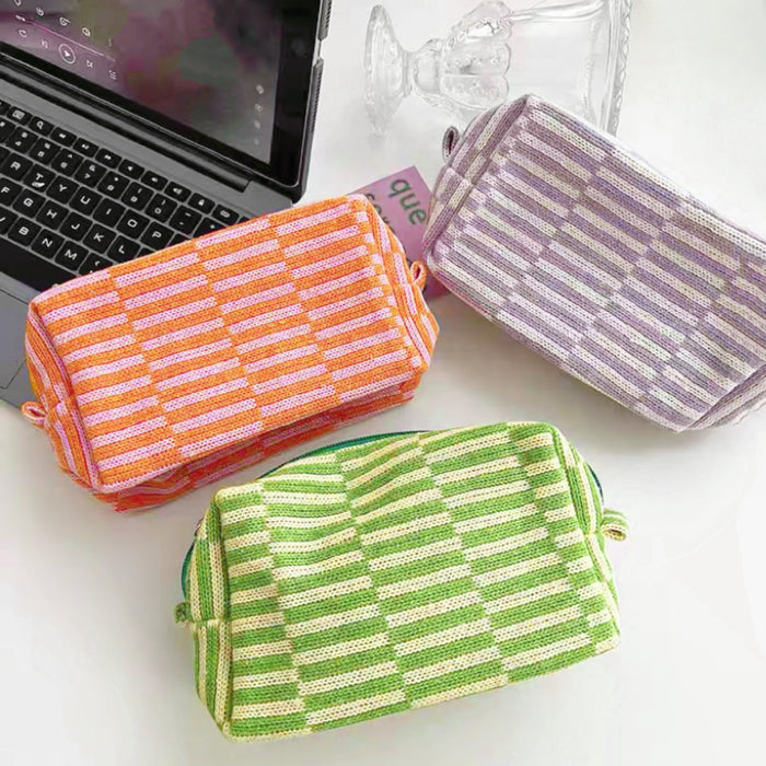 Flat lay of three striped knitted makeup bags in orange, green, and purple, made from blended yarn.