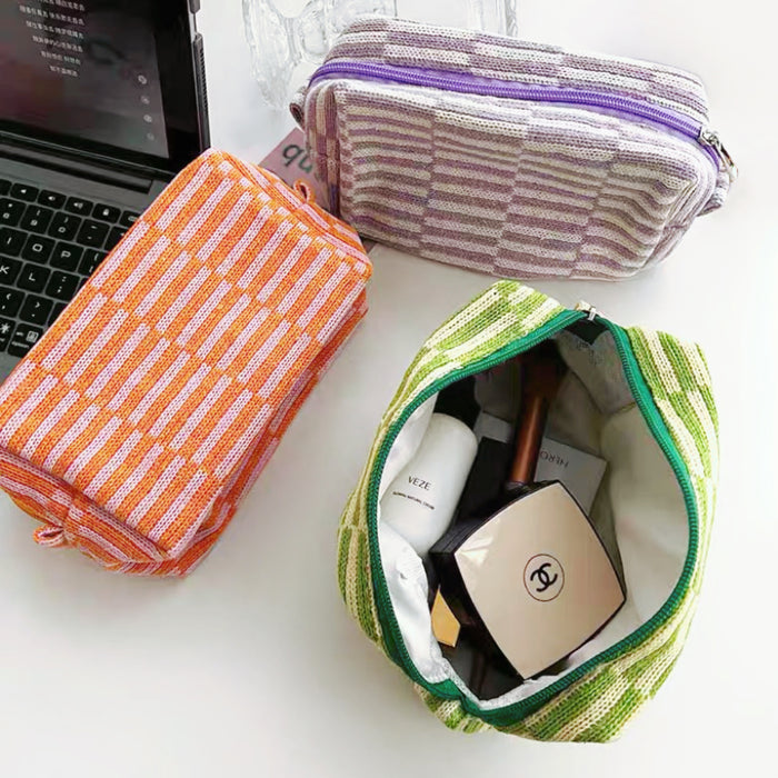 Angle view of three striped knitted makeup bags in orange, green, and purple, showcasing the inteior.