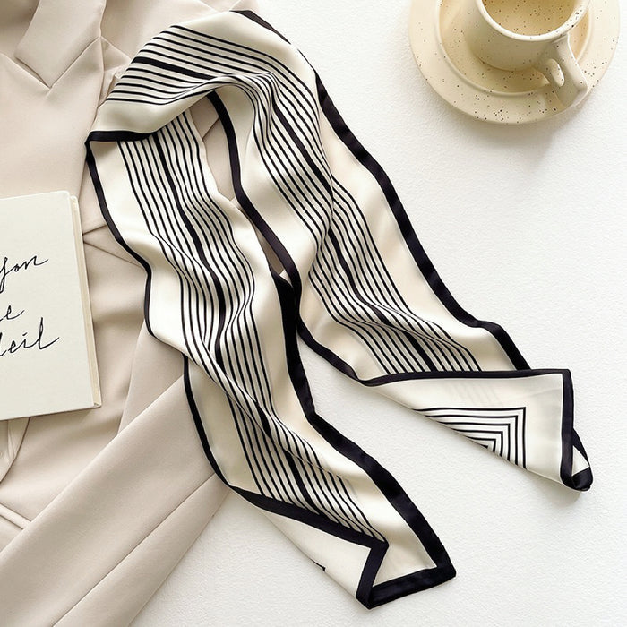 Angled view of White satin skinny scarf with black vertical stripes and border, draped on a beige blazer, easy.