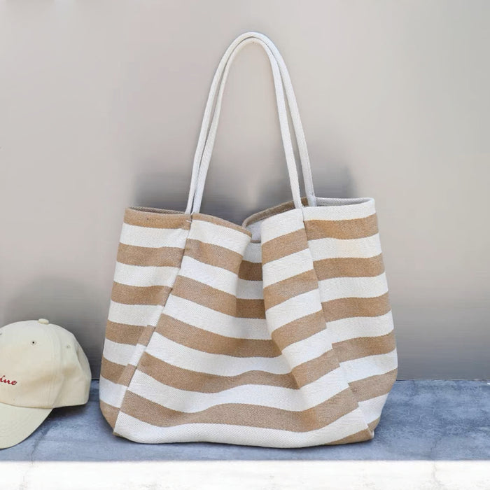 Close-up of Beige and white striped canvas tote bag with long straps, next to a cream baseball cap, ideal for errands.