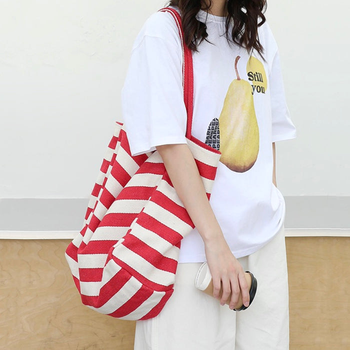 Model carrying a red striped tote bag on shoulder , ideal for city walks and gifting.