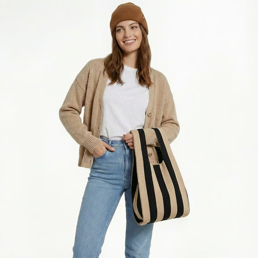 A woman wearing a brown cardigan and jeans holding a black and khaki stripe woven tote bag, showcasing French-chic style.
