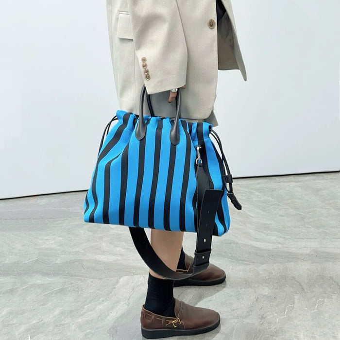 Model holding the blue and black striped bowling bag; high-contrast street style accessory for Athleisure Chic looks.