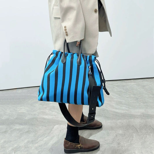 Model holding the blue and black striped bowling bag; high-contrast street style accessory for Athleisure Chic looks.