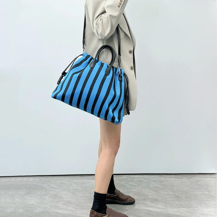 Side view of the blue striped bag on a model; showcases the spacious width and removable shoulder strap functionality.