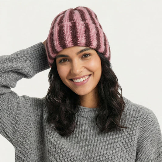 Smiling woman wearing a coral pink and brown striped fluffy knit beanie for a cozy winter look.
