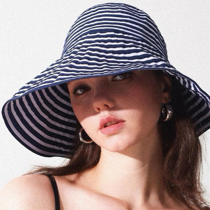 Woman wearing a navy and white striped wide brim bucket hat, perfect for stylish summer sun protection.