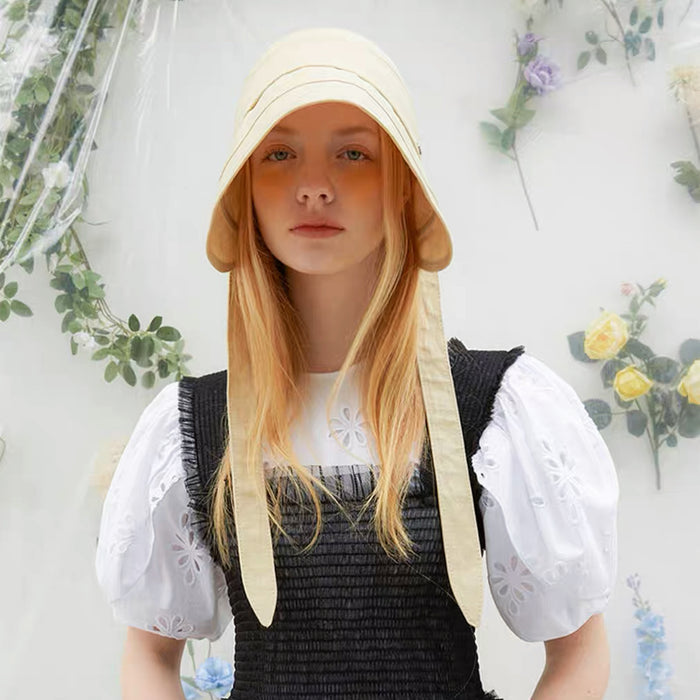Model wearing the cream yellow ribbon hat in a bright outdoor garden setting.