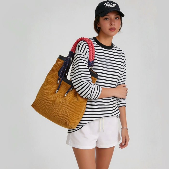 Model shoulder-carrying the corduroy tote bag, styled with a striped long-sleeve top and white shorts, outdoor casual look.