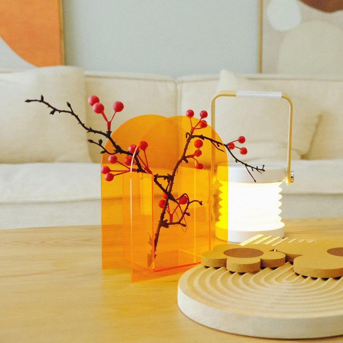 Front view of Modern orange acrylic vase with red berry branches inside and a portable white lantern.