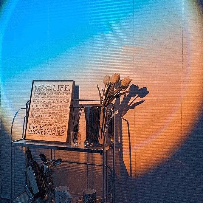 Sunset/Daybreak lamp casting warm, colorful light onto a wall with inspirational text and decorative items.