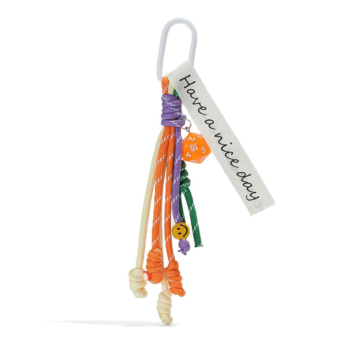 Front view of Polyester tassel bag charm with white carabiner, Have a nice day tag, orange dice, and smiley face.