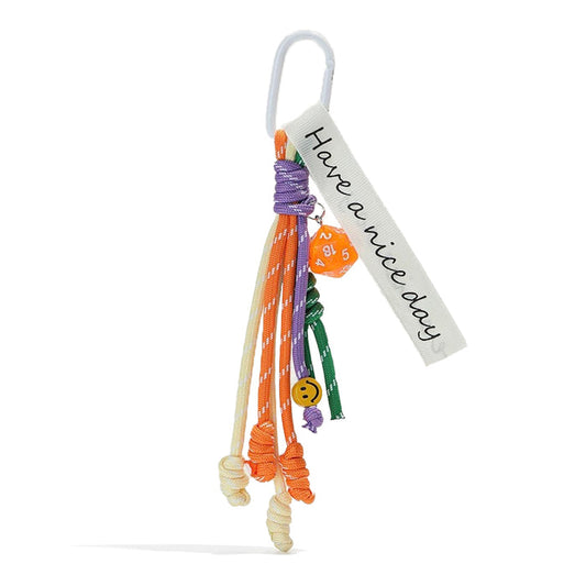 Front view of Polyester tassel bag charm with white carabiner, Have a nice day tag, orange dice, and smiley face.