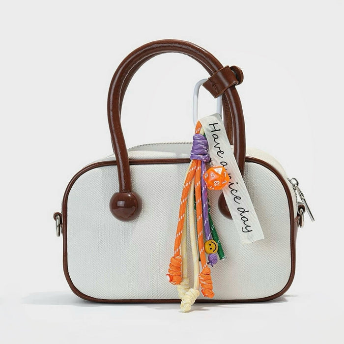 Orange Tassel Strings Bag Charm hanging on a beige handbag, great for winter looks and travel days.