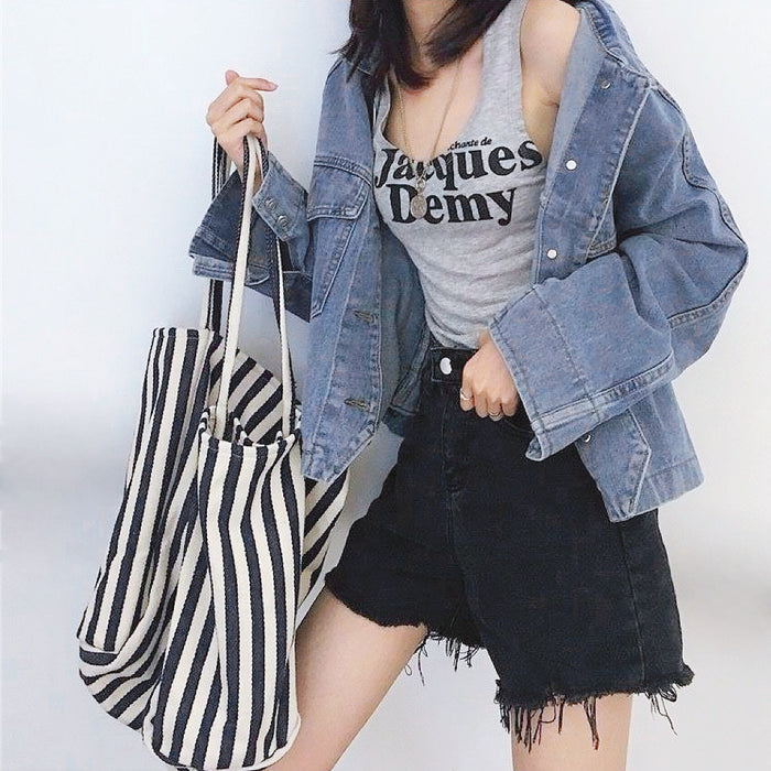 Woman holding a large white and black thin stripe canvas tote bag with shoulder strap.