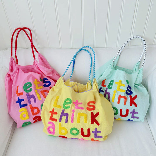 Front view of Three cotton tote bags in pink, yellow, and mint green with colorful embroidered.