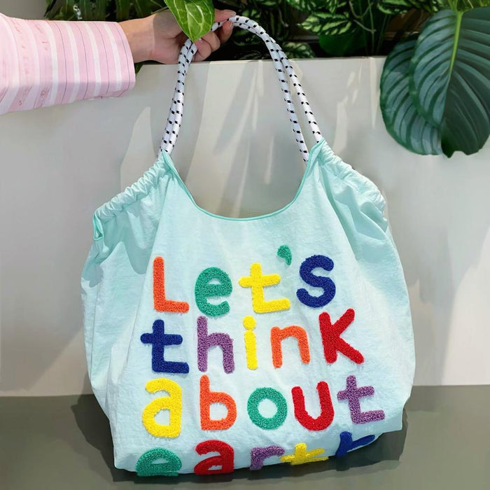 Angled view of mint green cotton tote bag with think about earth embroidery.
