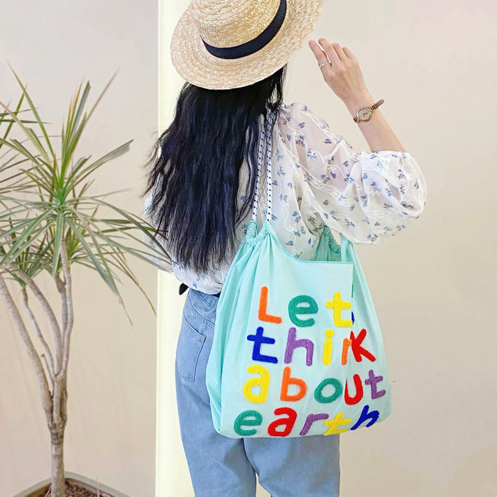 Model carrying a mint green Think About Earth Tote Bag on the shoulder, ideal for city walks and gifting.