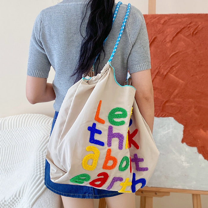 Angled view of Think About Earth Tote Bag in beige worn on model's shoulder, great for everyday carry and travel.