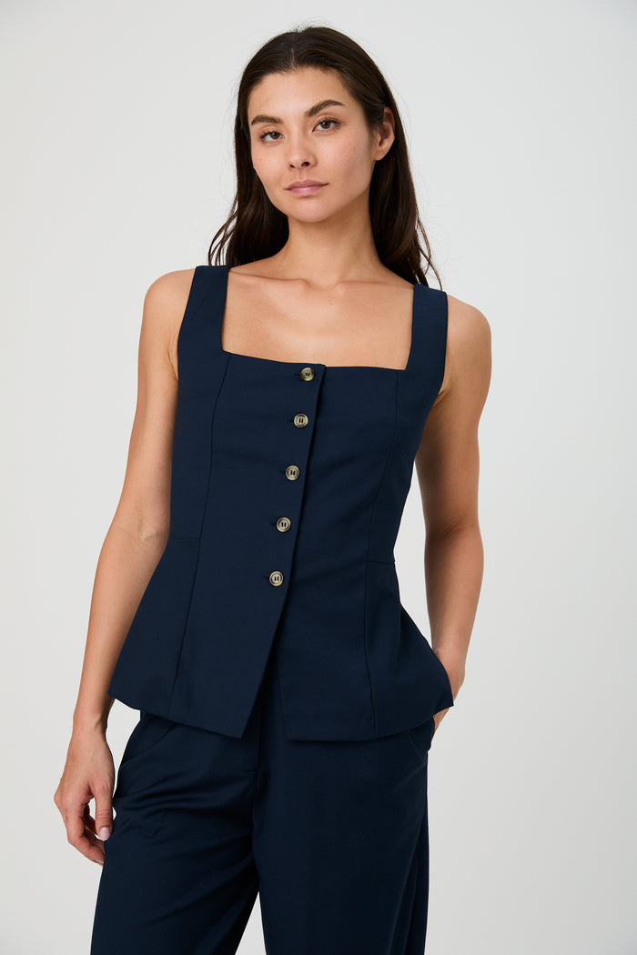Woman wearing a navy blue sleeveless blazer with buttons on a white background