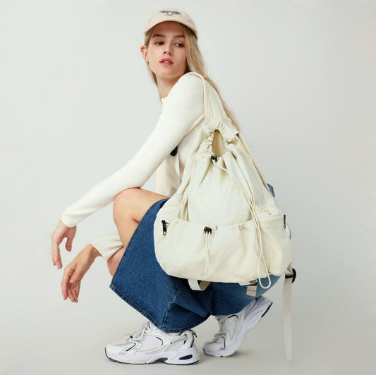 Model wearing white drawstring backpack; spacious design ideal for carrying books and laptops on campus.