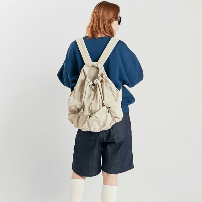 Model wearing cream backpack from behind; minimalist sporty look suited for active lifestyles and hiking.
