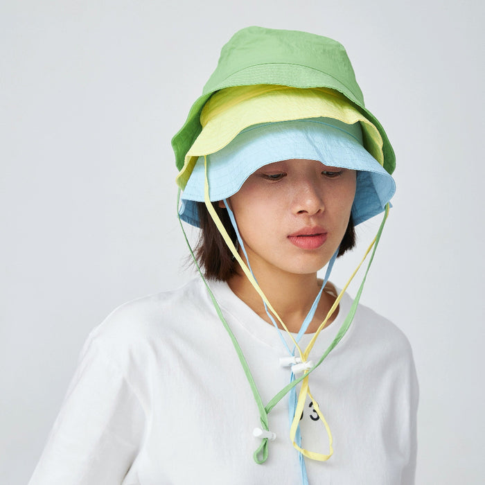 Model wearing three hats of different colors, stacked on top of one another.