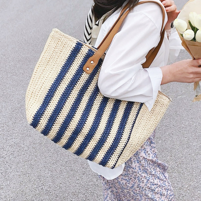 Model carrying a Vertical striped straw tote bag with blue and natural stripes on her shoulder.
