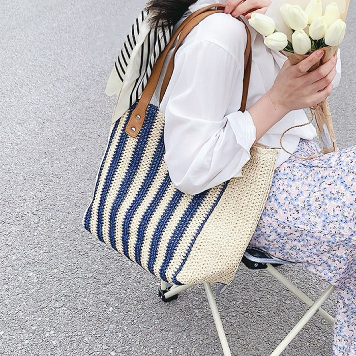 Model carrying a Vertical Striped Straw Tote Bag in blue, great for daily carry and travel.