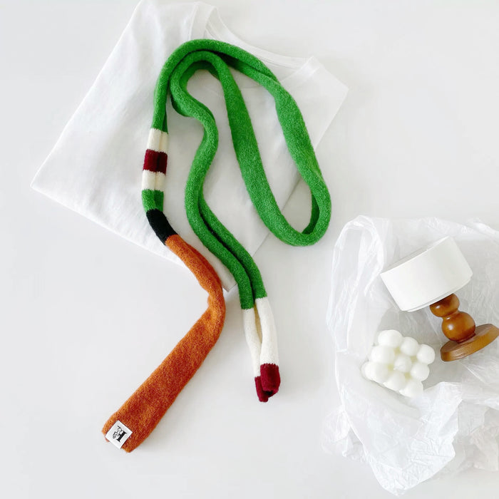 Angled view of colorblocked skinny polyester scarf in green, orange, white, and burgundy, easy for travel.