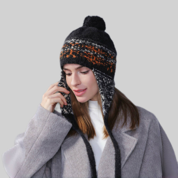 Woman wearing black wool-acrylic ear flap hat with orange Fair Isle patterns and a playful pom-pom.