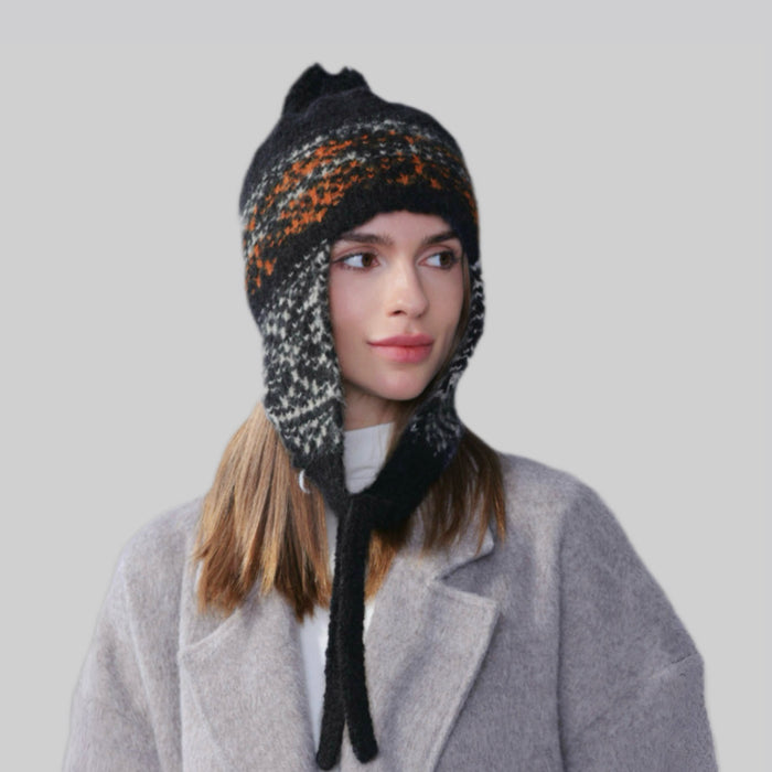 Woman wearing a black, orange, and white Winter Isle ear flap hat with secure chin ties for cold-weather protection.