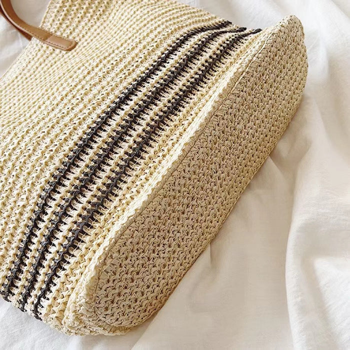 Close-up of Beige woven straw tote bag with black stripes, showcasing the bottom.