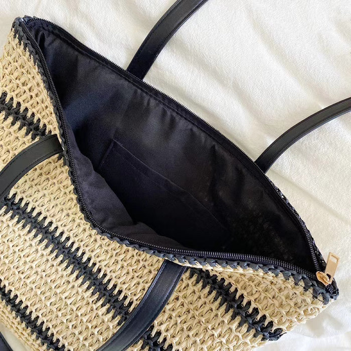 Angled view of Woven straw tote bag with black stripes, black PU leather straps, and a zippered black interior.